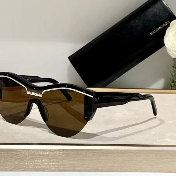Flat lay of Balenciaga Ski cat-eye frame sunglasses next to branded case and accessories