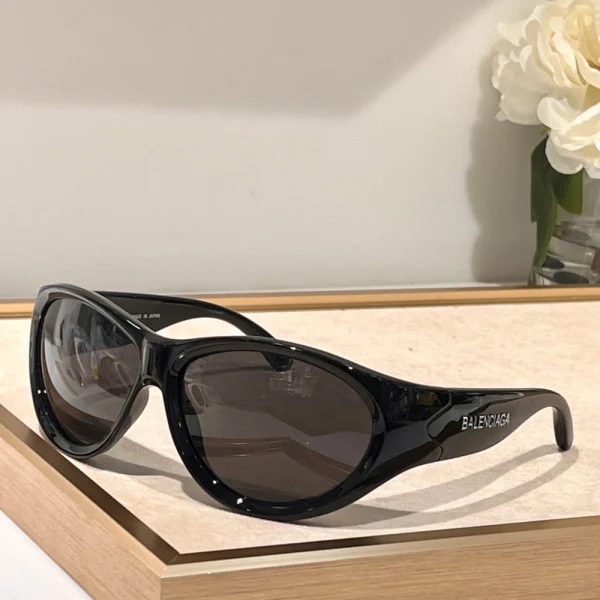 Balenciaga Swift oval sunglasses displayed on smooth surface with soft lighting and branded case in background