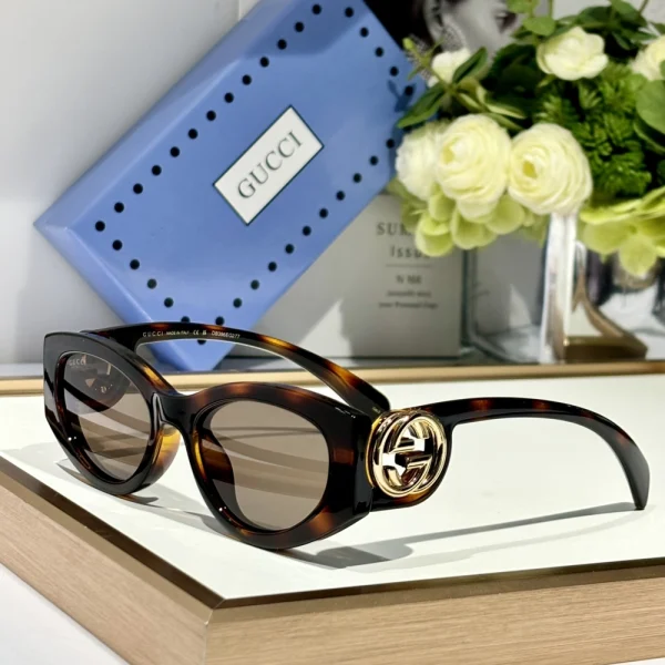 Gucci cat-eye frame sunglasses placed on white surface, paired with branded case and cloth