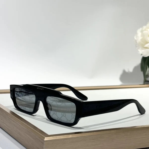 Top-down shot of Gucci sunglasses with rectangular frame, next to accessories and travel pouch