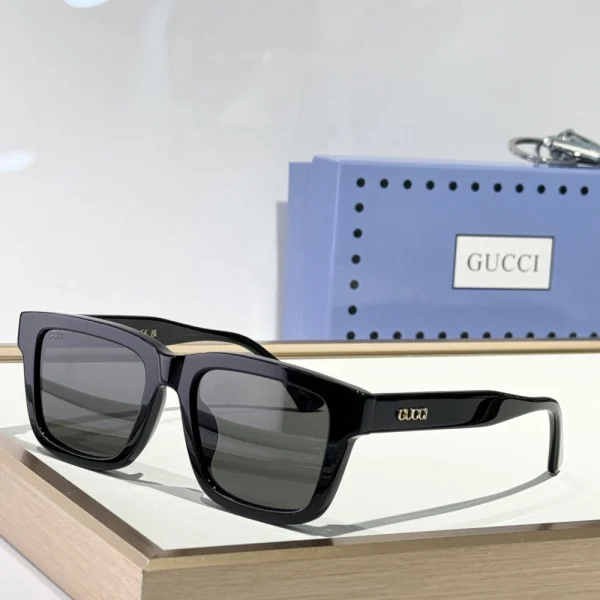 Gucci rectangular-frame sunglasses resting on soft fabric surface, highlighting slim profile and luxury logo