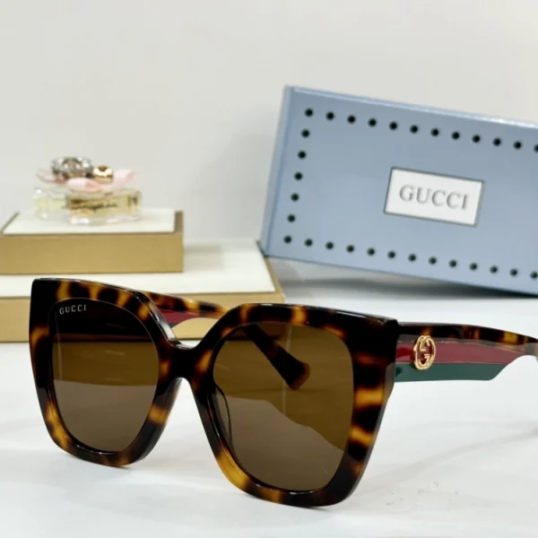Minimalist flat lay of Gucci Square-frame sunglasses next to branded hard case and cloth
