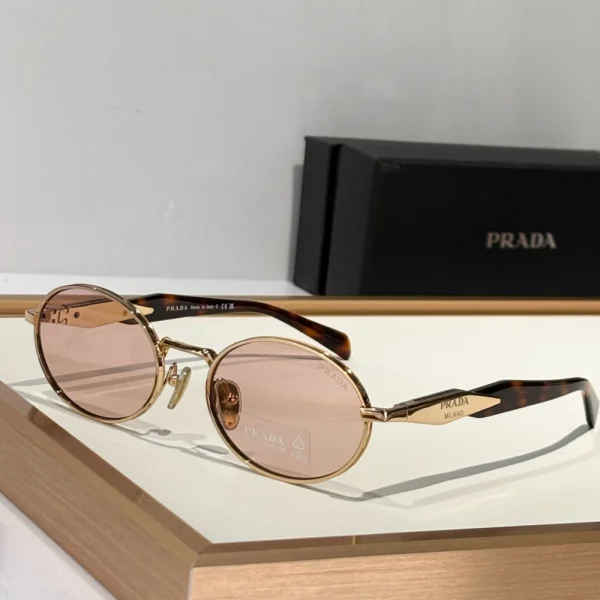 Prada Eyewear Collection sunglasses with gold metal frame and tinted lenses, laid on soft white fabric