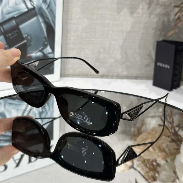 Black Prada triangle logo sunglasses placed beside branded case and packaging on a clean studio background