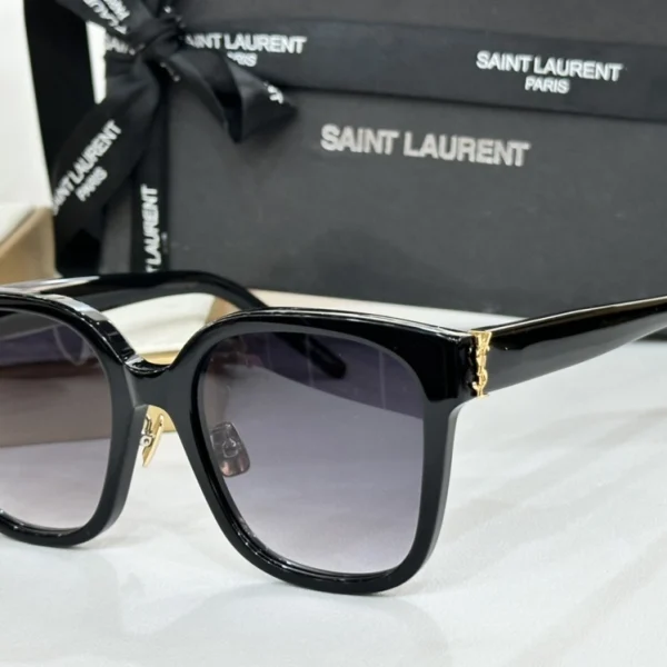 Black Saint Laurent SL M40 Monogram sunglasses placed diagonally on marble surface under natural light