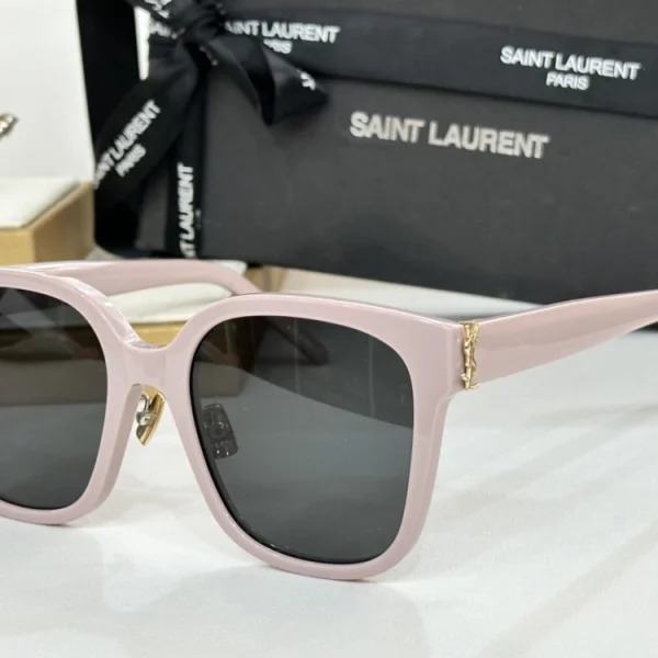 Saint Laurent SL M40 sunglasses with glossy black frame and iconic YSL monogram, captured on soft beige fabric