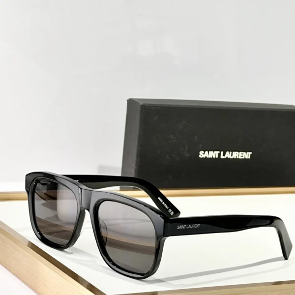 Saint Laurent SL 558 sunglasses with sleek square black frame and dark lenses, styled on a clean white tabletop