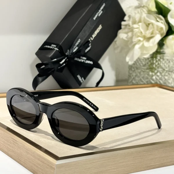 Black Saint Laurent SL M136 sunglasses resting on beige velvet fabric under soft natural lighting
