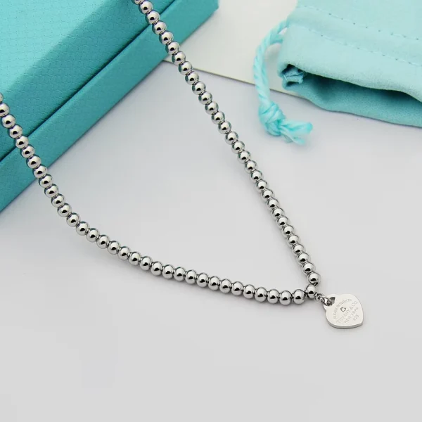 Side angle of the Bead Necklace highlighting smooth silver beads and engraved heart tag